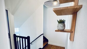 Een houten trap met een zwarte leuning, een hangende lamp en een plankje met een potplant.