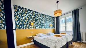 Een kamer met twee bedden, een behang met patroon, een hanglamp en een raam met uitzicht.