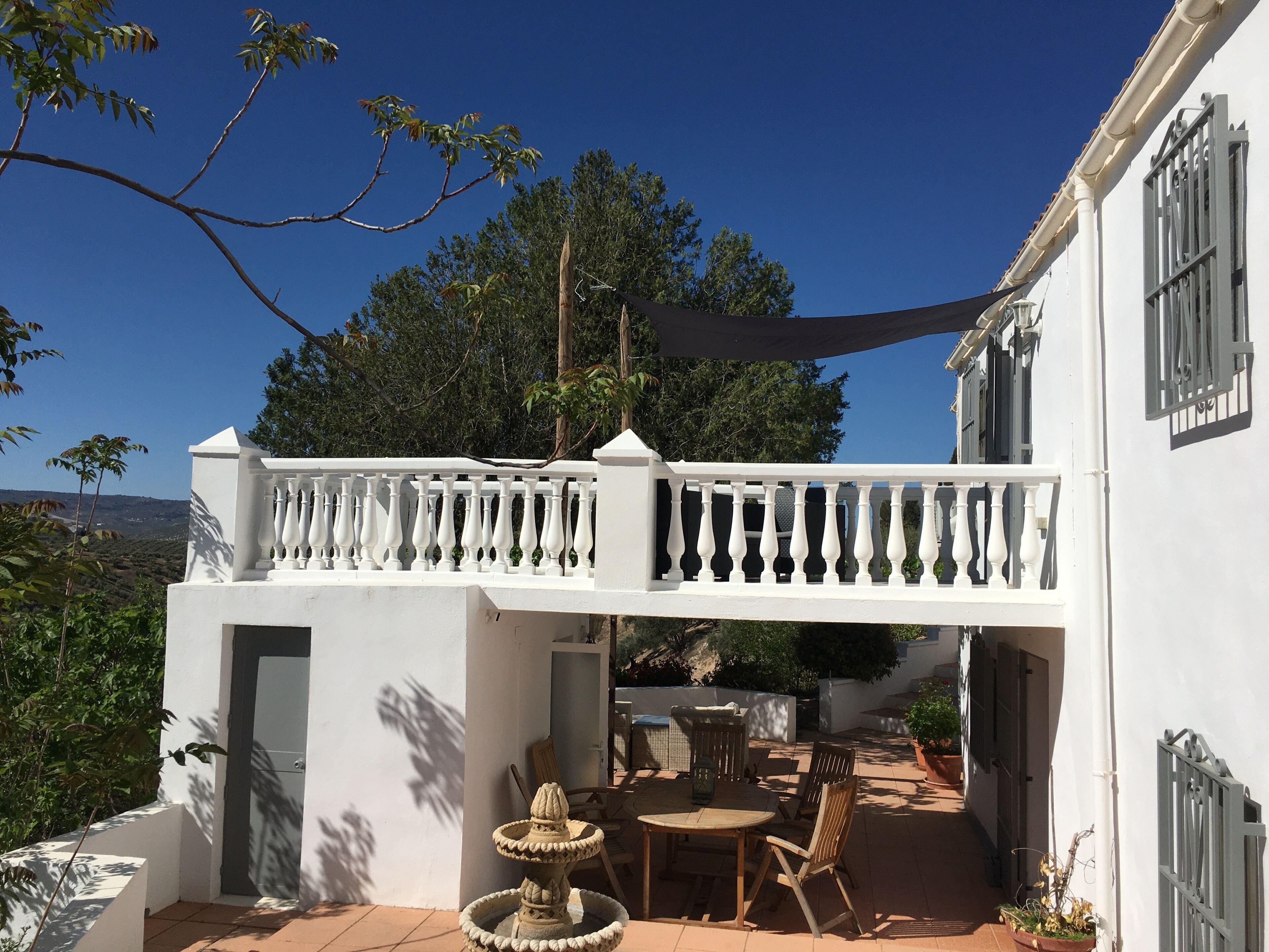Un edificio blanco con balcón, mobiliario exterior y una fuente decorativa.