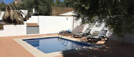 Une piscine avec un escalier, entourée d’une terrasse carrelée et de chaises longues.