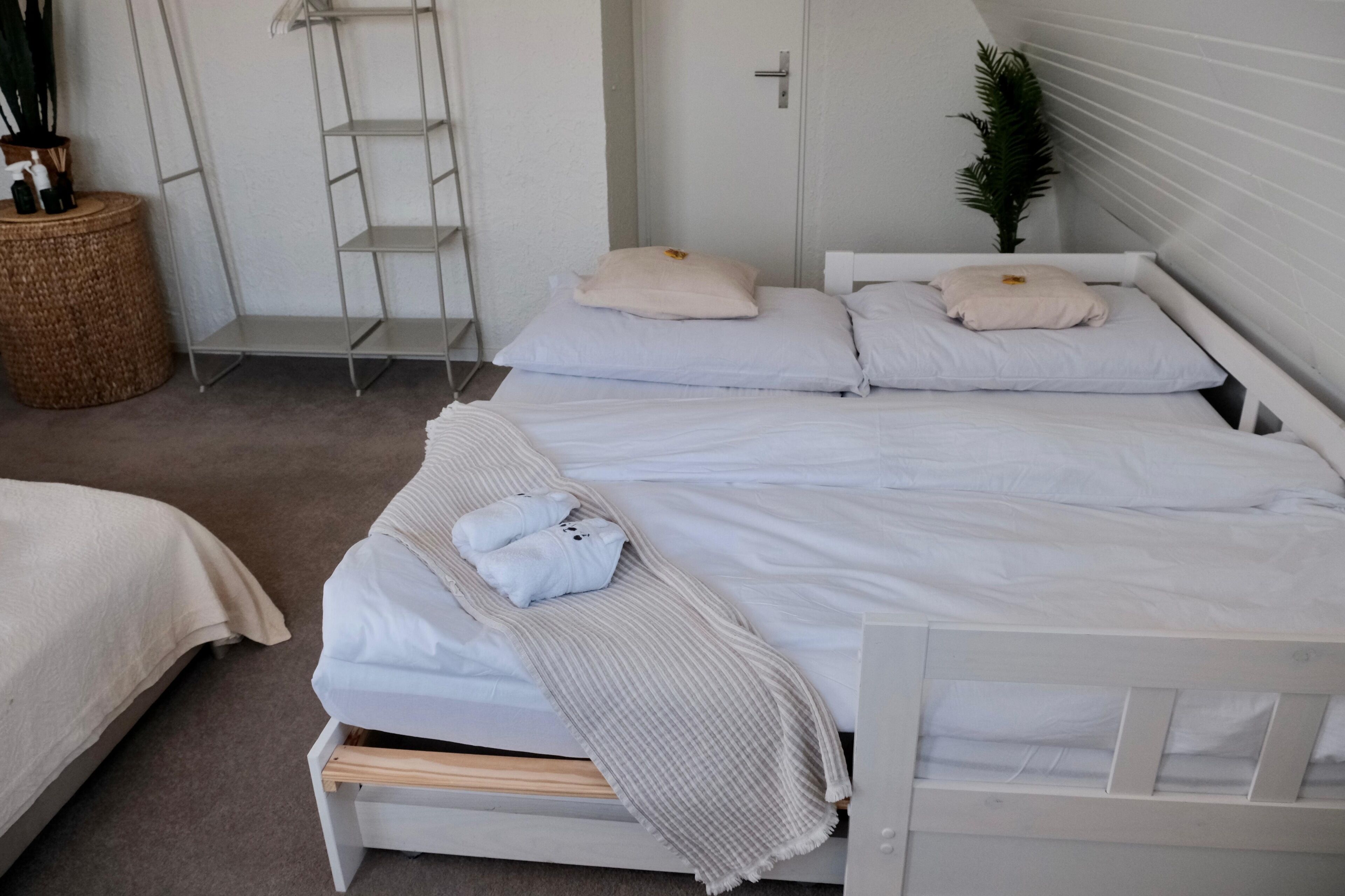 Une chambre à coucher avec deux lits, chacun agrémenté de draps et d’oreillers blancs, d’une tête de lit en bois, d’une petite table de chevet et d’un panier en osier.