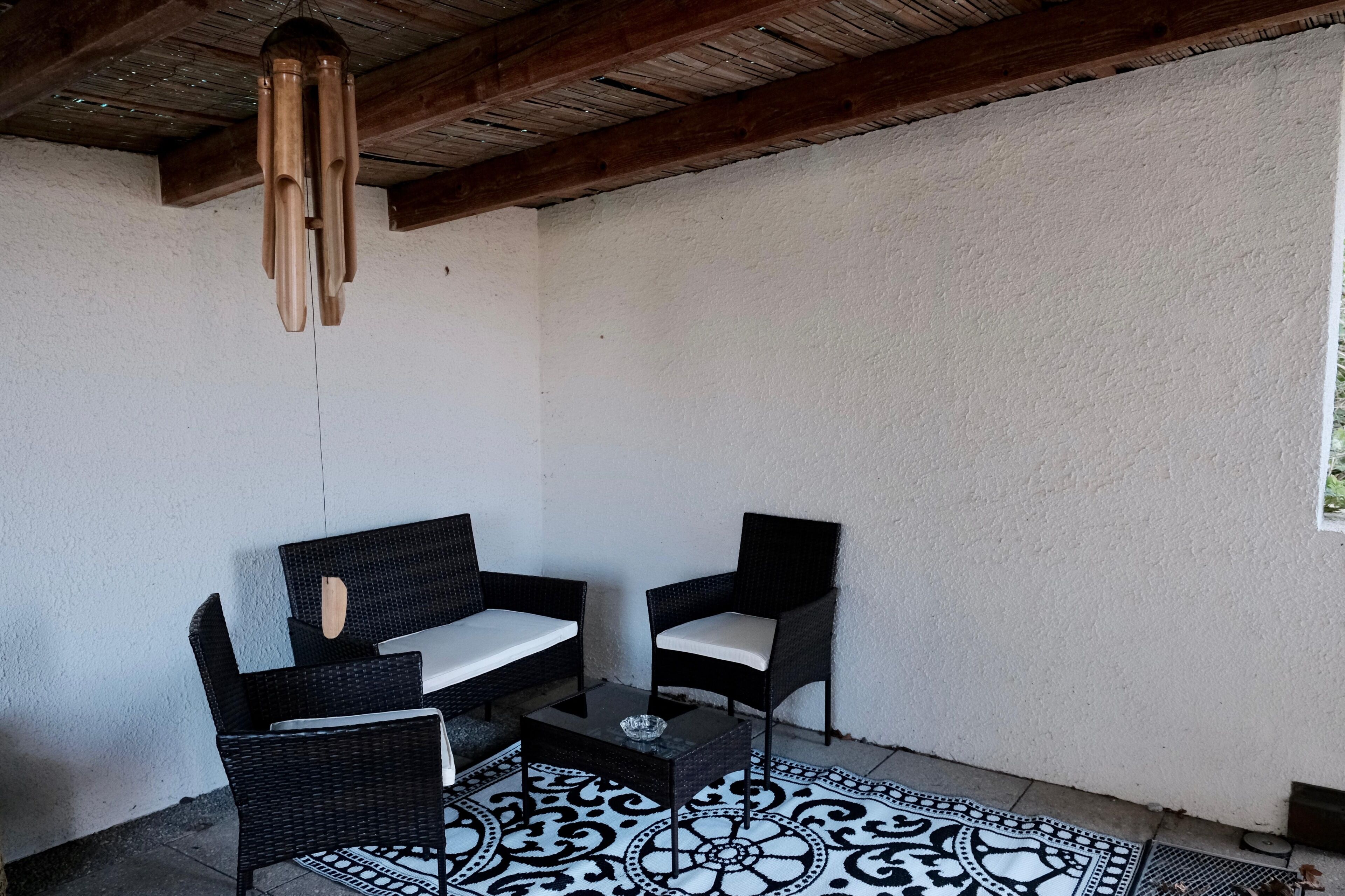 Une terrasse avec deux fauteuils en osier, une petite table et un luminaire suspendu.