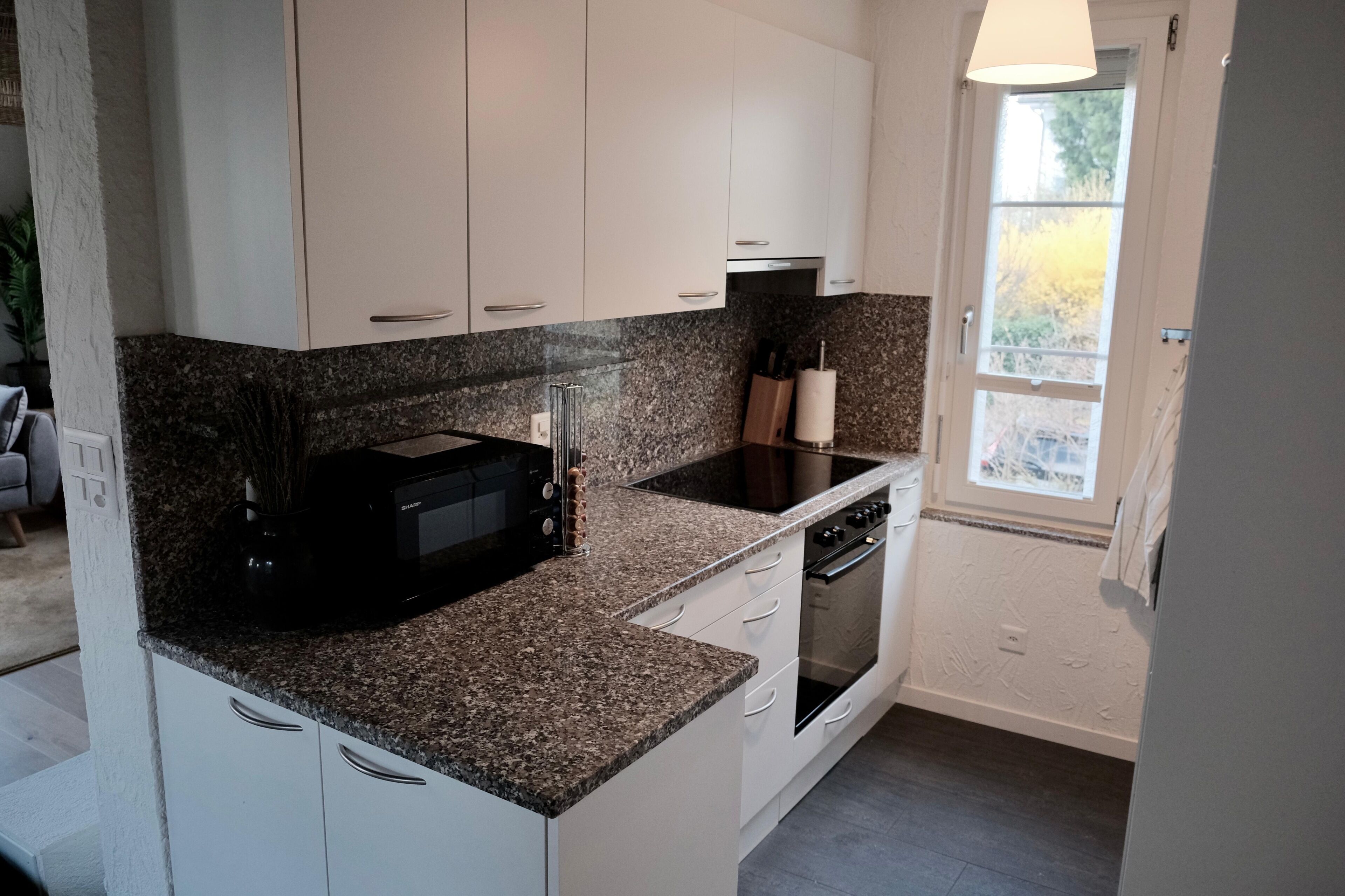 A compact kitchen with white cabinets, a granite countertop, a built-in microwave, a stove, and a window providing natural light.