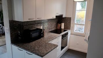 A compact kitchen with white cabinets, a granite countertop, a built-in microwave, a stove, and a window providing natural light.