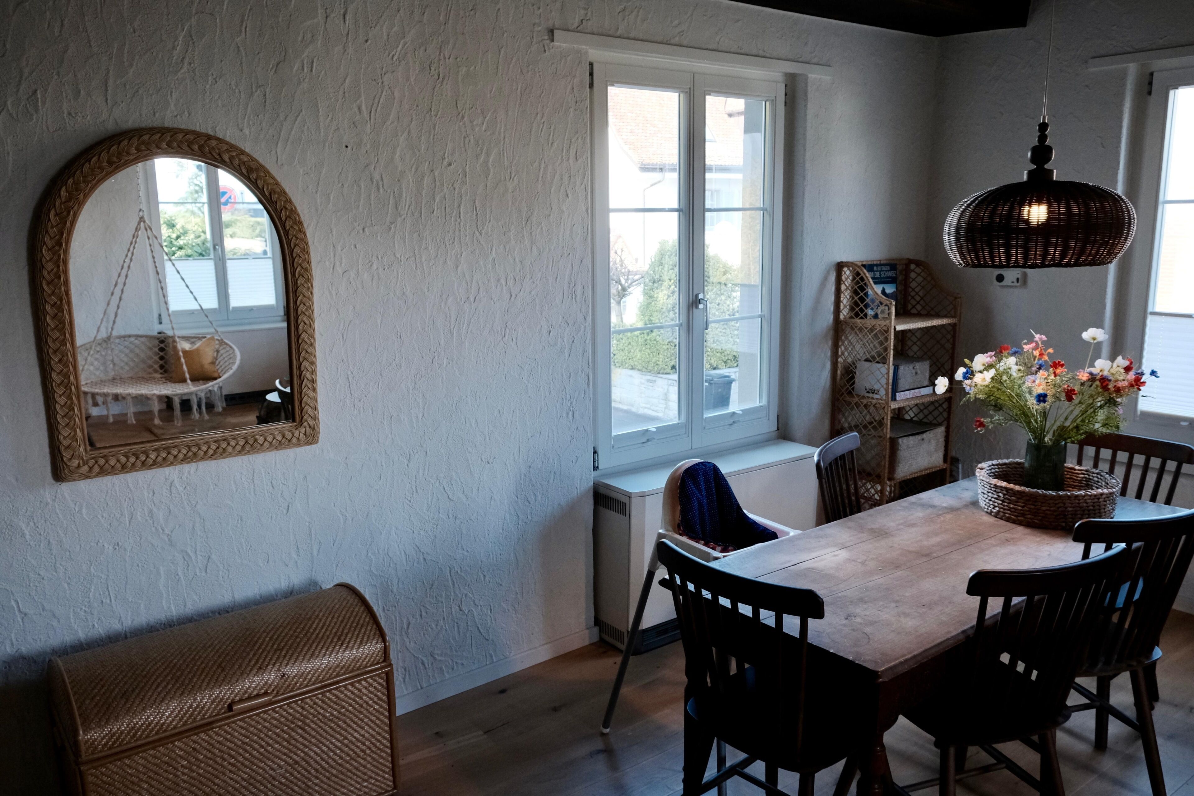 A dining area with a wooden table, chairs, a hanging light fixture, and a large mirror.
