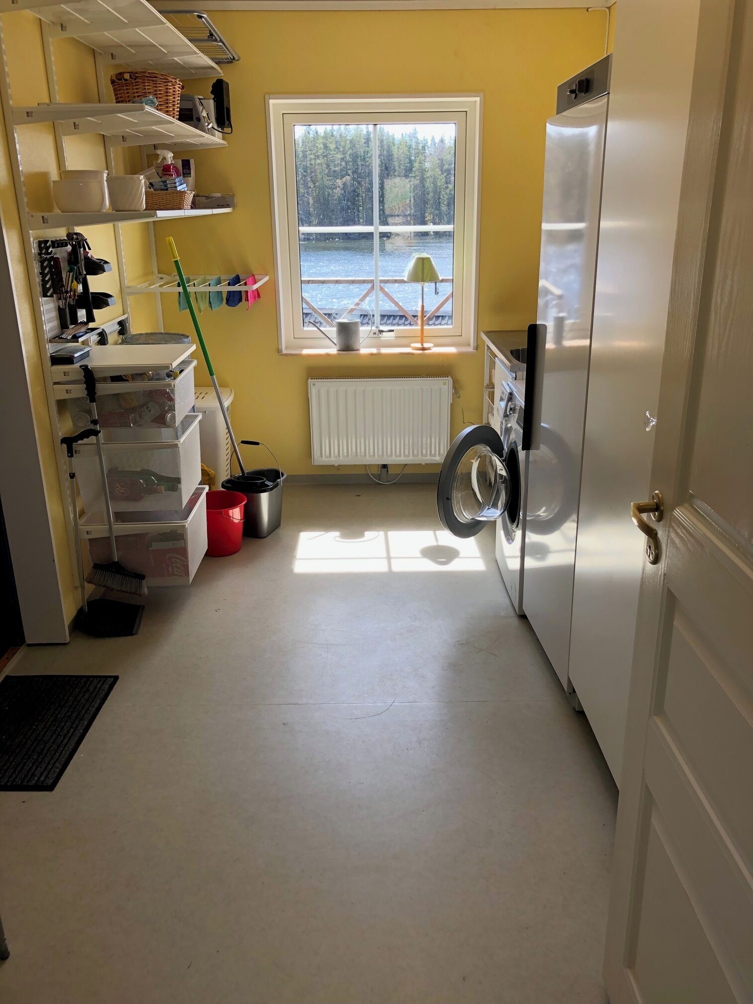 A kitchen with a refrigerator, a window with a view, and storage shelves.