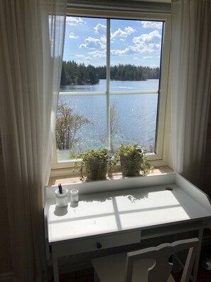 Ein Fenster mit Blick auf einen See und Bäume, ein weißer Schreibtisch mit Pflanze und eine Tasse mit Trinkhalm.