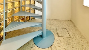 Uma escada em espiral com estrutura metálica azul e um parapeito de vidro com padrão quadriculado.