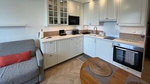 A compact kitchen with white cabinets, a microwave, a coffee maker, and a built-in oven. - Studio Méva (Courseulles-sur-Mer)