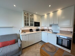 A compact kitchen with white cabinets, a microwave, a coffee maker, and a built-in oven. - Studio Méva (Courseulles-sur-Mer)