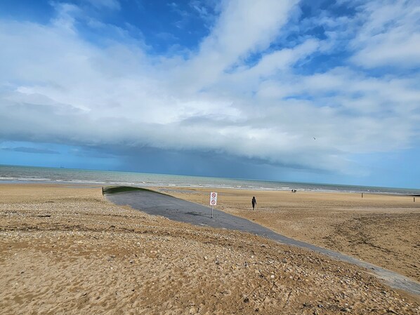A beach with a paved walkway, a no swimming sign, and a distant ship on the horizon. - Studio Méva (Courseulles-sur-Mer)