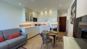 A compact living space with a sofa, dining table, chairs, kitchen area, and a refrigerator. - Studio Méva (Courseulles-sur-Mer)