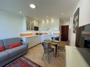 A compact living space with a sofa, dining table, chairs, kitchen area, and a refrigerator. - Studio Méva (Courseulles-sur-Mer)