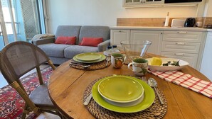 A dining table with plates, a cup, and cutlery. There is a sofa and a chair in the background. - Studio Méva (Courseulles-sur-Mer)