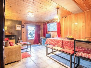 Un interior de madera con una mesa de comedor, asientos tipo banco, una chimenea y una ventana con cortinas.