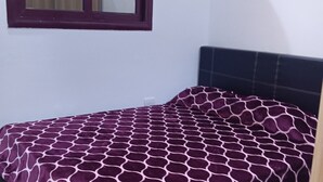 Una cama individual con colcha estampada, cabecero oscuro y ventana con marco de madera.