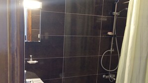 Un baño con lavabo, paredes de azulejos oscuros, ducha con cortina y grifo visible.