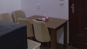 Habitación con una mesa de madera, sillas color beige, un dispositivo electrónico negro, una caja de pañuelos y una puerta.