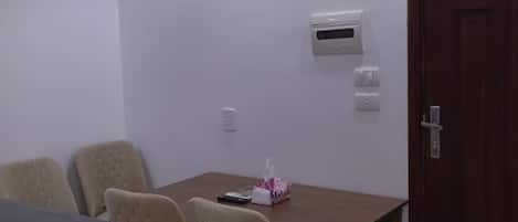 A room with a wooden table, beige chairs, a black electronic device, a tissue box, and a door.