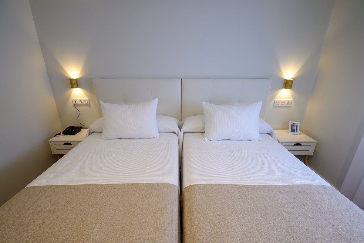 A double room with two beds, bedside lamps, a phone, and a small table.