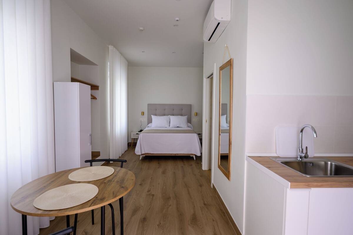 A hotel room with a bed, bedside table, and a kitchenette area.