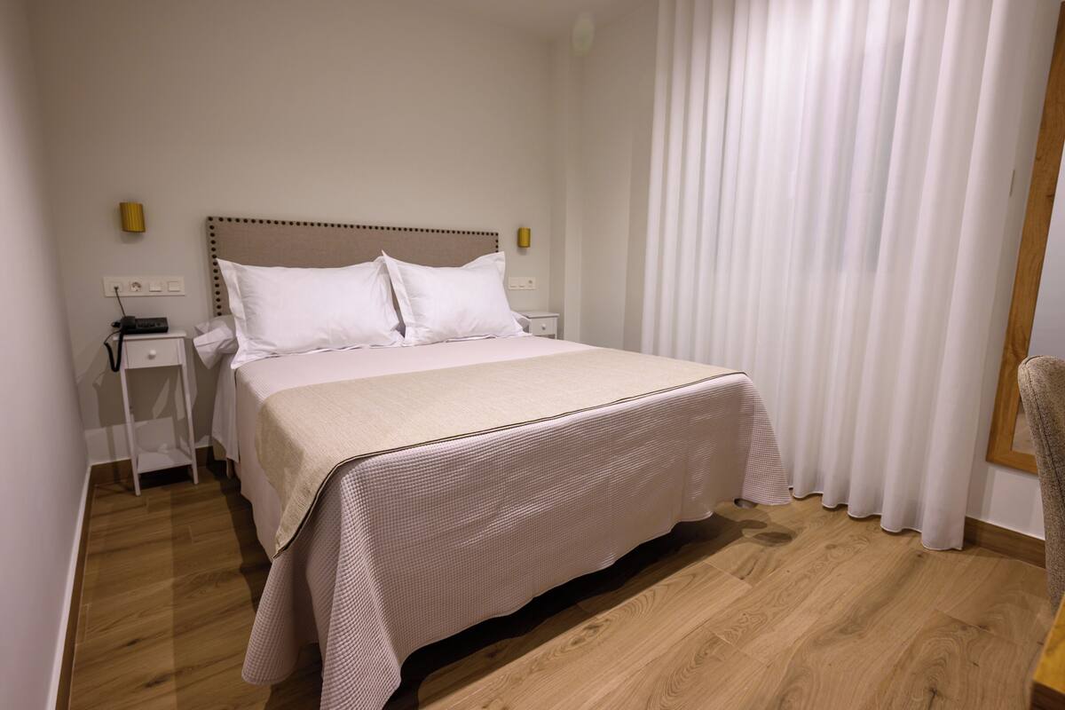 A hotel room with a bed, bedside tables, a lamp, and a window with curtains.