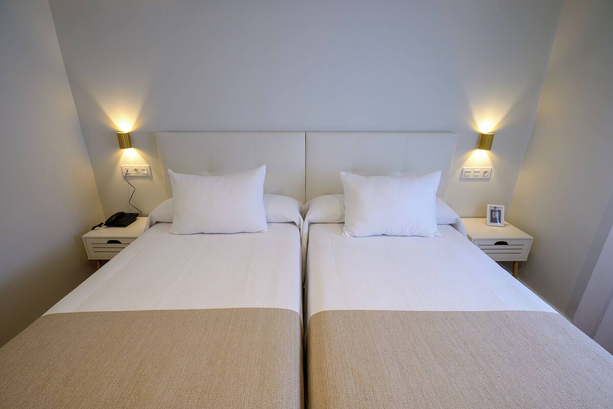 A double room with two beds, bedside lamps, a phone, and a small table.