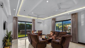 Ein modernes Wohnzimmer mit Flachbildfernseher, braunen Ledersofas, Deckenventilator und großen Fenstern.