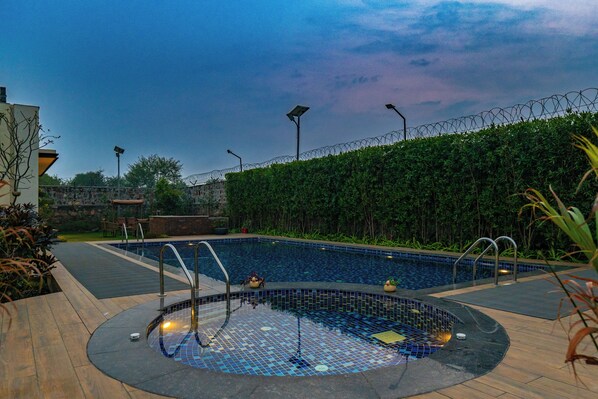 A swimming pool with a tiled edge, surrounded by a hedge and a stone wall. - ELIVAAS Prassanam Vatika 2 BHK Hillside Villa with Private Pool (Faridabad)