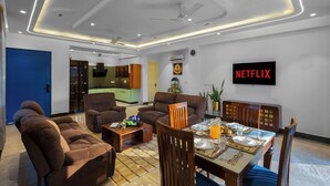 Ein modernes Wohnzimmer mit Sofas, einem Esstisch, einem Fernseher und einer Küche im Hintergrund.