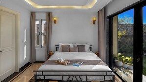 Ein Schlafzimmer mit einem Bett, Nachttischlampen, einem Deckenventilator und Blick auf Grün hinter einem großen Fenster.