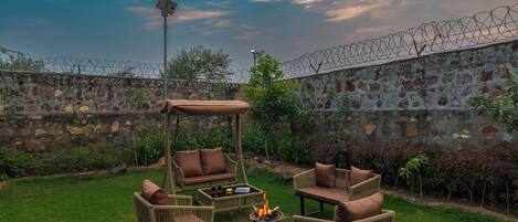 A patio with wicker furniture, a fire pit, and a stone wall with barbed wire.