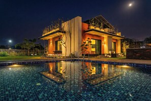 A modern house with a swimming pool, surrounded by greenery and a clear night sky. - ELIVAAS Prassanam Vatika 2 BHK Hillside Villa with Private Pool (Faridabad)