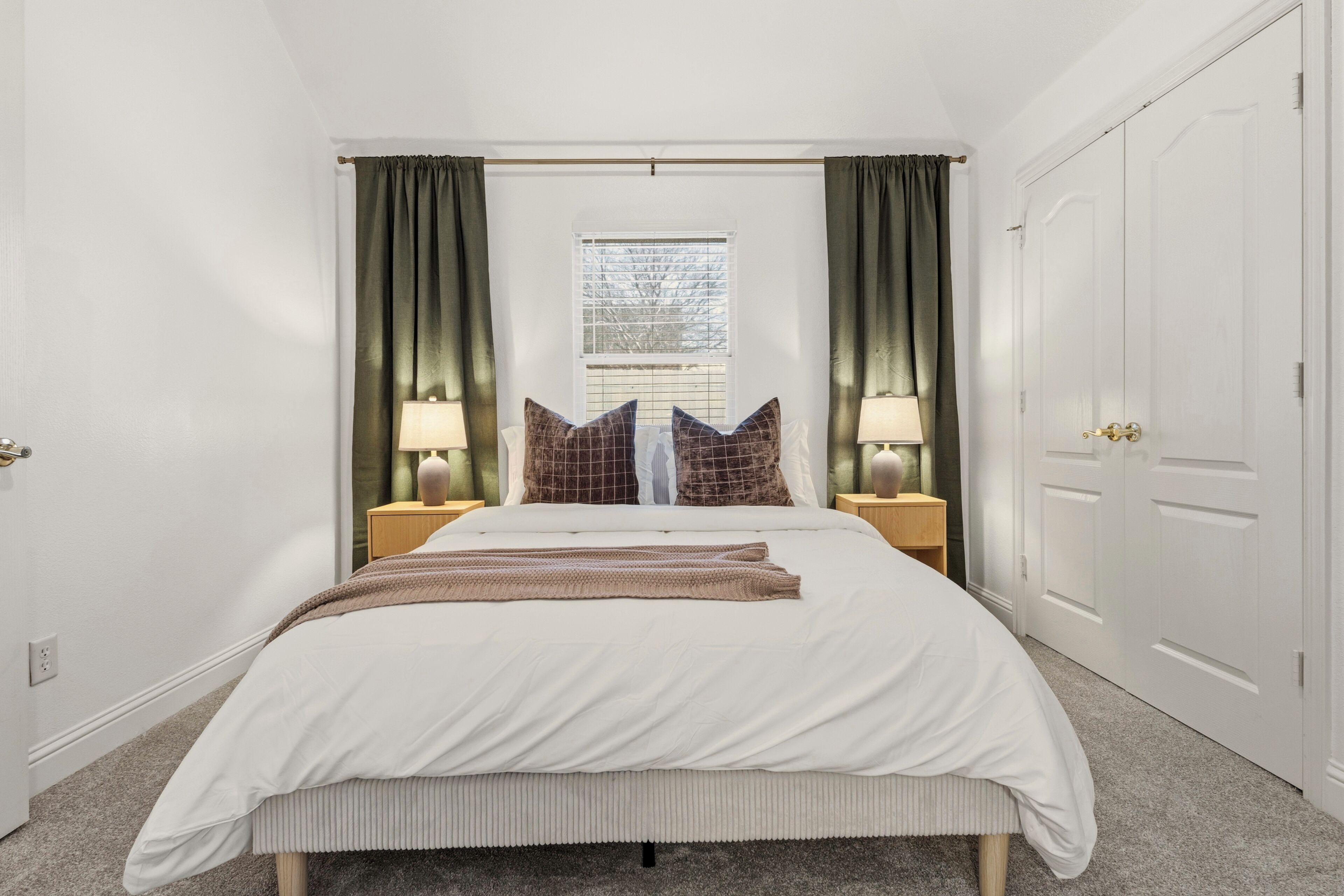 Een slaapkamer met een bed, twee nachtkastjes, een raam met gordijnen en een kledingkast.