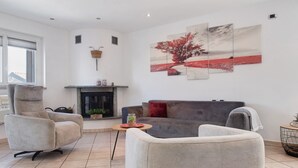 Un salon avec une cheminée, un canapé, deux fauteuils et un tableau au mur.