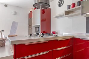 Una cocina moderna con encimera roja, electrodomésticos de acero inoxidable y salpicadero blanco.