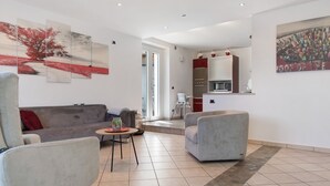 Un salon moderne avec un canapé gris, une table basse ronde et un fauteuil gris. On y trouve également un coin cuisine avec un meuble rouge et un réfrigérateur blanc.