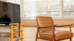 A room with a television on a glass shelf, a leather chair, and a window with blinds. - Lovely 2BR flat w balcony, Golders Green tube 5min (London)