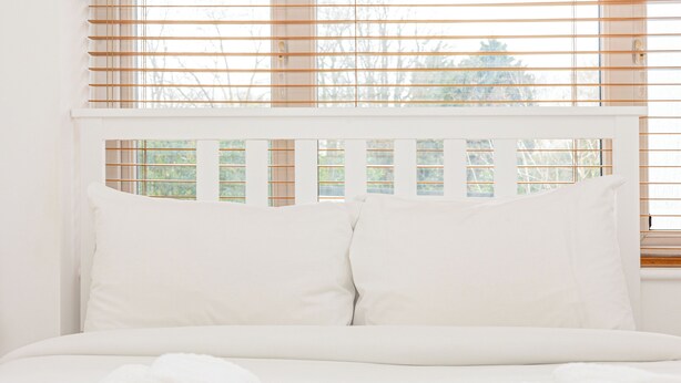 A bed with white bedding and pillows, a window with blinds, and a view of trees outside. - Lovely 2BR flat w balcony, Golders Green tube 5min (London)