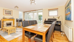 A spacious living room with a wooden dining table, comfortable seating, a fireplace, a television, and a piano. - Lovely 2BR flat w balcony, Golders Green tube 5min (London)