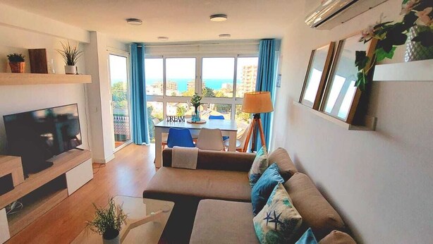 Una sala de estar moderna con una televisión de pantalla plana, un sofá, una mesa de comedor y vista al mar.