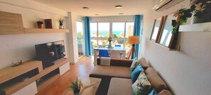Un salon moderne doté d’un téléviseur à écran plat, d’un canapé, d’une table à manger et offrant une vue sur la mer.