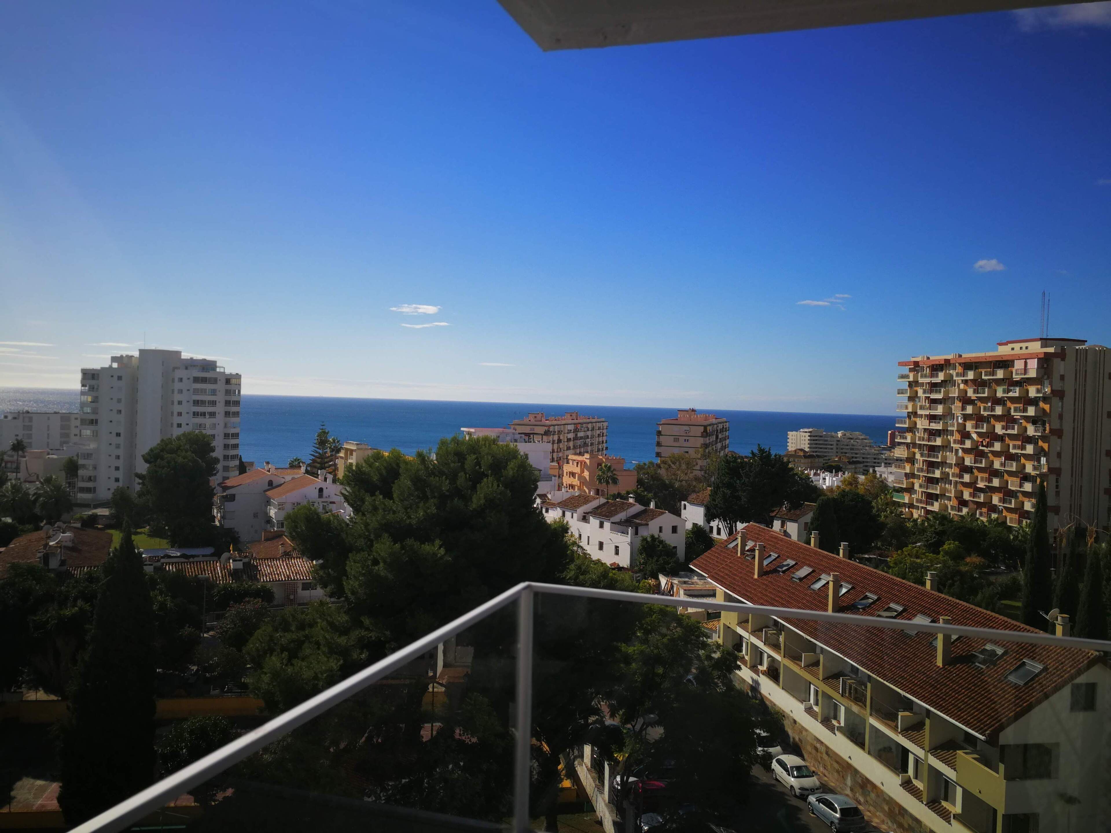Un paisaje urbano costero con varios edificios, incluyendo apartamentos de gran altura y casas más pequeñas, con una vista despejada del mar.