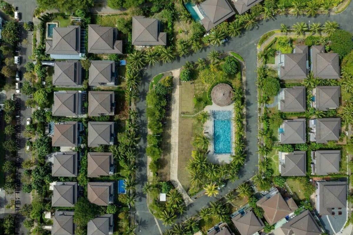 An aerial view of a residential area with multiple houses, a swimming pool, and surrounding greenery.