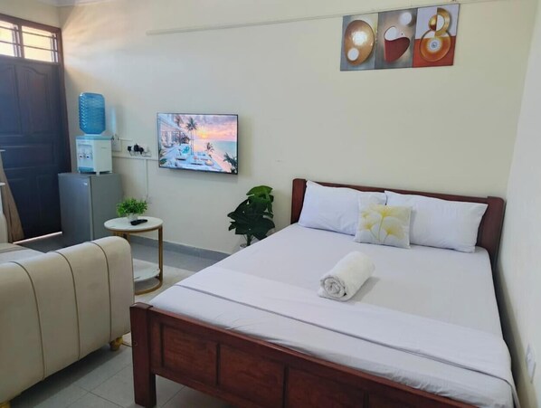 Habitación de hotel con cama, escritorio, silla, dispensador de agua, televisión y un cuadro en la pared.