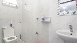 Une salle de bain avec des toilettes, un lavabo, une douche et un seau rouge.