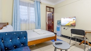 Une chambre d’hôtel avec un lit, un canapé bleu recouvert de tissu, une petite table avec une télécommande, un distributeur d’eau et un téléviseur fixé au mur.