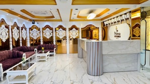 A hotel lobby with a reception desk, plush seating, marble flooring, and ornate ceiling details.