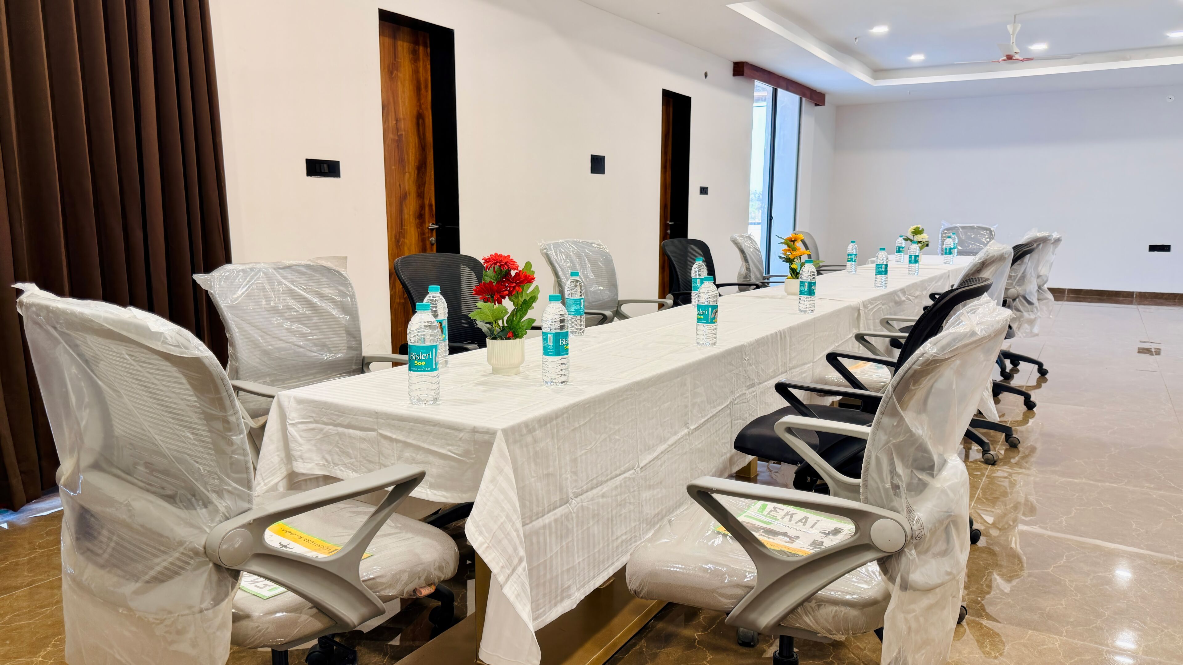 A conference room with a long table, chairs, water bottles, and a vase with flowers.