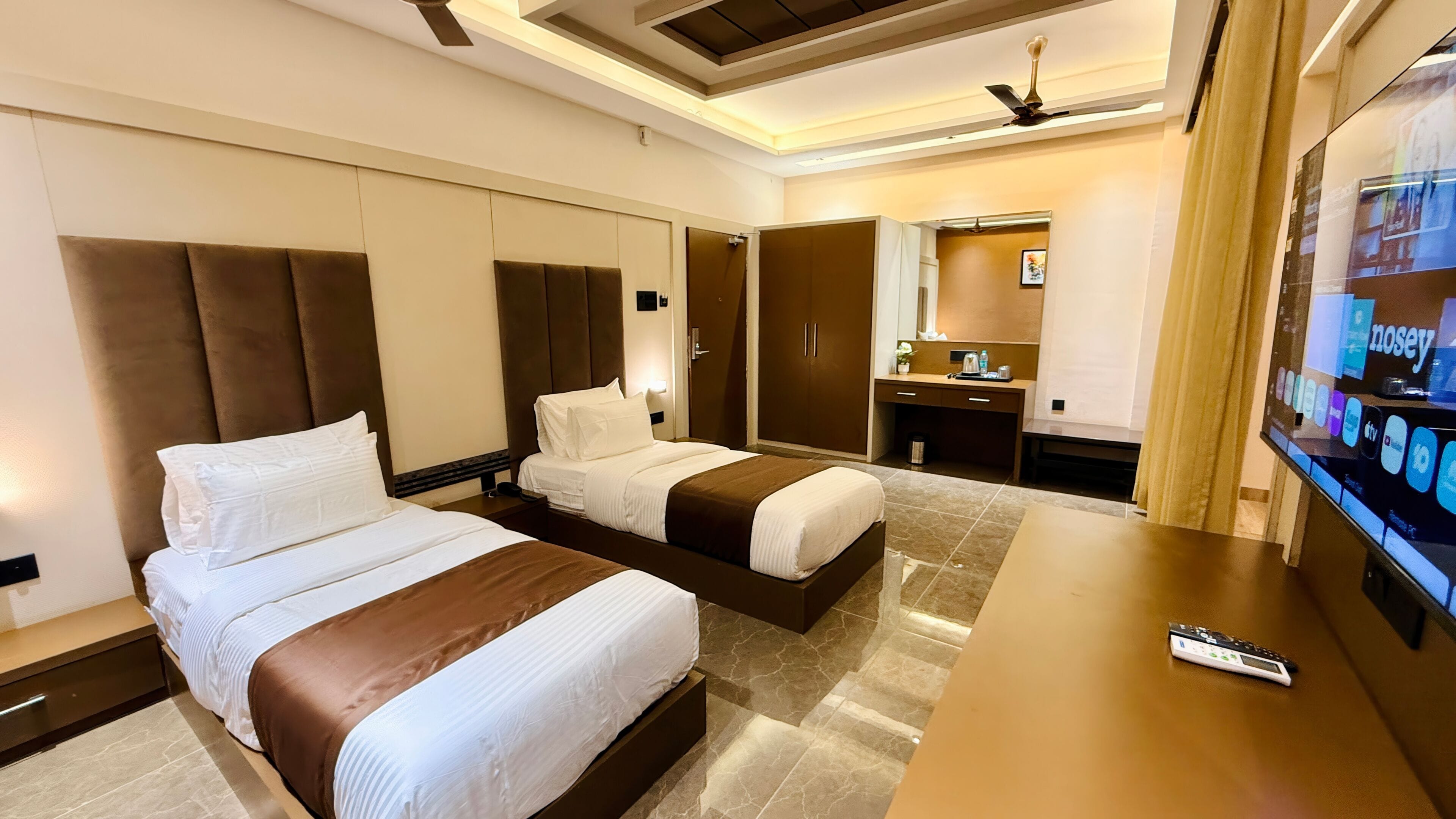 A hotel room with two beds, a desk, a TV, and a bathroom.